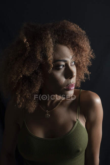 Affascinante modella afroamericana con i capelli ricci che distoglie lo sguardo in uno studio buio — Foto stock