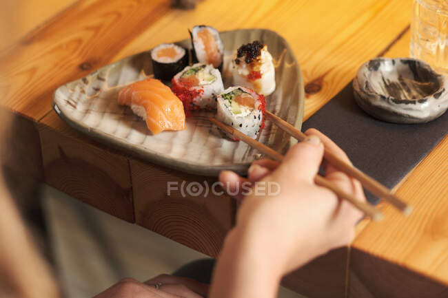 Dall'alto ritagliato femminile irriconoscibile mangiare sushi gustoso nel ristorante giapponese mentre seduto al tavolo di legno — Foto stock