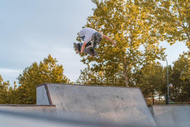 Teenage boy jumping with skateboard and showing stunt on ramp in skate park — Stock Photo