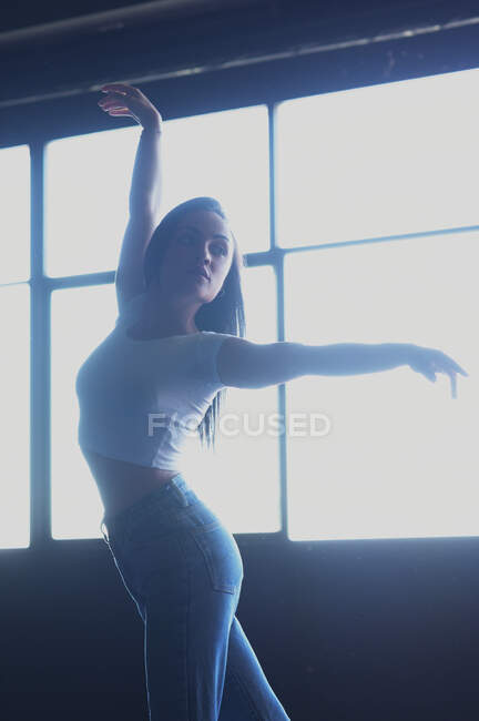 Giovane femmina in jeans che balla mentre distoglie lo sguardo sul pavimento alla luce del sole — Foto stock