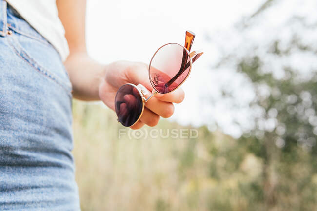 Cultivo de mujer anónima sosteniendo unas gafas de sol en su mano - foto de stock