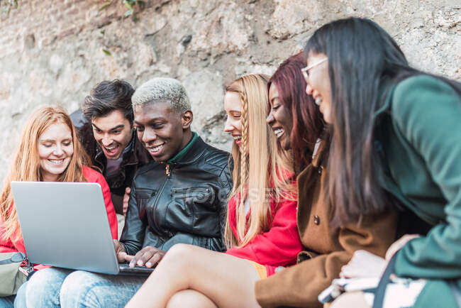 Compagnia di studenti diversi che fanno i compiti insieme mentre usano netbook in strada — Foto stock