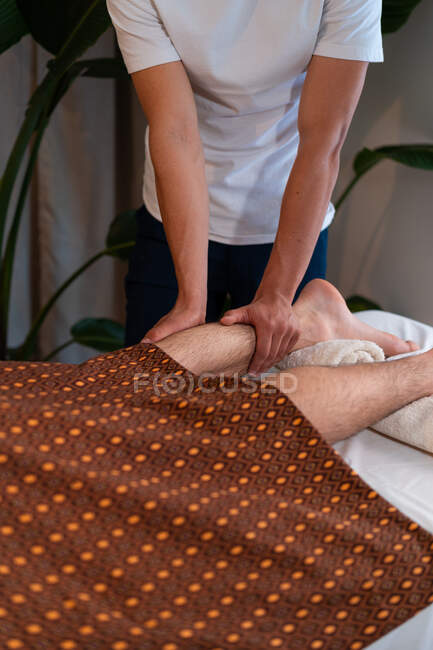 Thérapeute méconnaissable masser les jambes du client masculin tout en faisant un massage thaï dans le centre de spa — Photo de stock