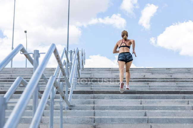 Неузнаваемая женщина тренируется подниматься по лестнице на открытом воздухе, вид сзади — стоковое фото