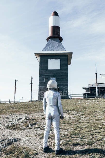 Homem de corpo inteiro em traje espacial em pé em solo rochoso contra cerca de metal e foguete listrado em forma de antenas no dia ensolarado — Fotografia de Stock