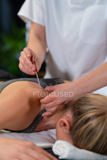 Unrecognizable physiotherapist inserting needle into shoulder of relaxed female patient during acupuncture session in clinic — Stock Photo