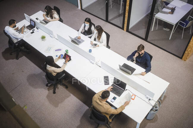 From above of company of people sitting at table and using laptops while working in coworking space — Stock Photo