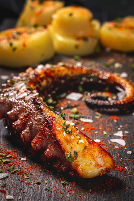 Сверху жареный осьминог щупальце и куски картофеля подаются со специями на черной доске на столе — стоковое фото