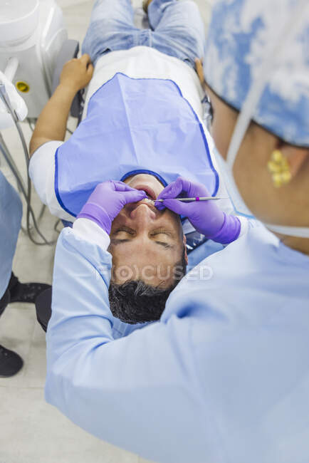 Estomatóloga femenina en uniforme y máscara respiratoria curando dientes de paciente masculino en el hospital - foto de stock