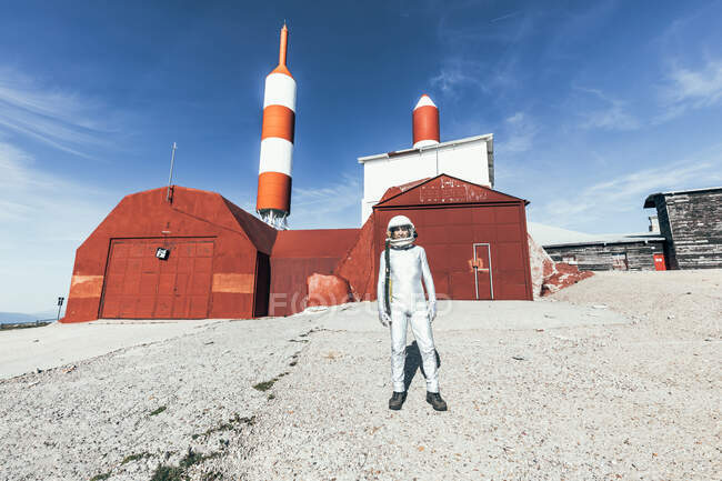 Full body man in spacesuit standing on rocky ground against striped rocket shaped antennas on sunny day — Stock Photo