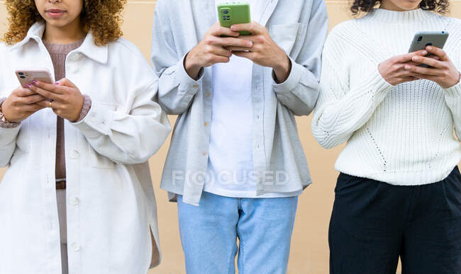 Homem de colheita e mulheres com cabelos cacheados em pé na fila e usando telefones em vício — Fotografia de Stock