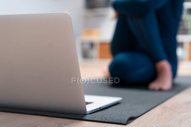 Cropped unrecognizable flexible young female yoga instructor doing half lord of the fishes pose in front of laptop screen during online class in fitness studio — Stock Photo