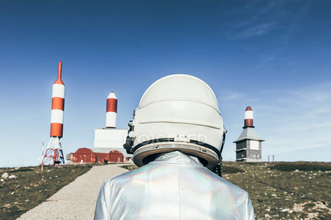 Uomo vista posteriore in tuta spaziale in piedi su terreno roccioso contro le antenne a forma di razzo a strisce nella giornata di sole — Foto stock