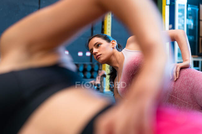 Fit sportswomen em activewear de pé olhando para longe na prancha lateral pose durante o treinamento no chão no ginásio — Fotografia de Stock