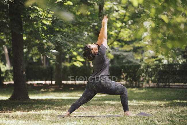 Seitenansicht einer übergewichtigen Frau, die in Ashta Chandrasana-Pose steht, während sie Yoga auf Matte im Sonnenlicht praktiziert — Stockfoto