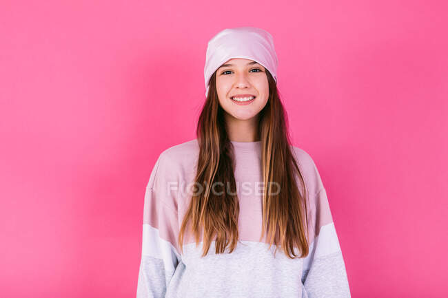 Glückliche Teenagerin mit braunen Haaren und Kopftuch, die das Krebsbewusstsein repräsentiert, blickt in die Kamera auf rosa Hintergrund — Stockfoto