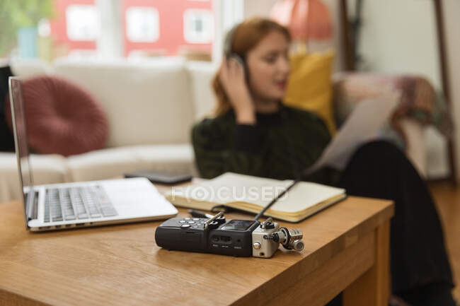 Сучасний аудіореєстратор, розміщений на дерев'яному столі на тлі розмитого жіночого радіо хоста в навушниках для запису подкасту — стокове фото
