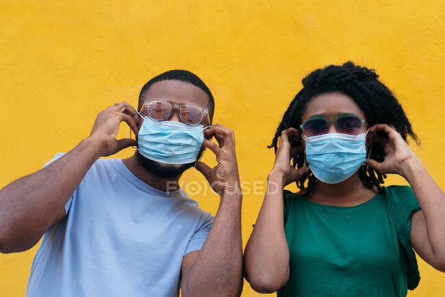 Black couple with mask posing on yellow background and looking at camera — Stock Photo