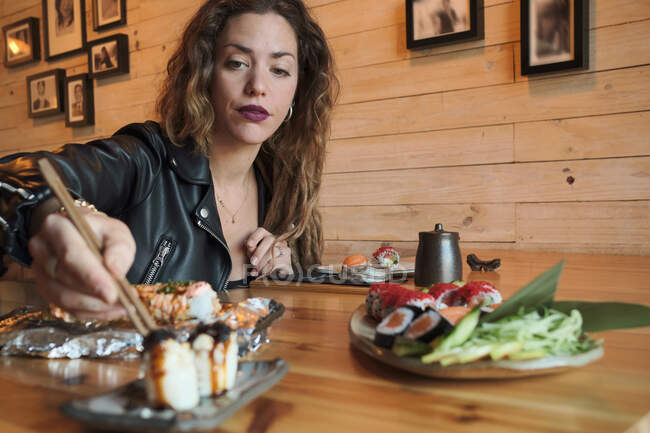 Mujer comiendo sushi sabroso en el restaurante japonés mientras está sentado en la mesa de madera - foto de stock