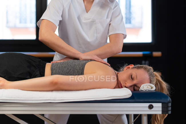 Ritagliato massaggiatrice irriconoscibile sorridente e massaggiare le spalle della donna mentre si lavora in clinica fisioterapia — Foto stock