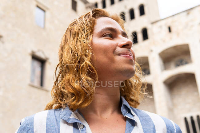 Dal basso tranquillo maschio felice con i capelli lunghi in piedi in strada e godendo di libertà guardando altrove — Foto stock