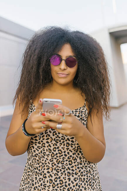 Jeune femme afro avec des lunettes de soleil bavarder avec son téléphone intelligent — Photo de stock