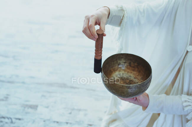 Crop woman playing singing bowl with wooden striker during spiritual practice — Stock Photo