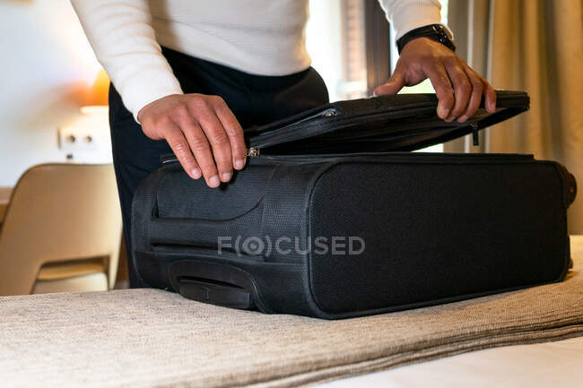 Crop anonimo viaggiatore maschio bagagli apertura posto sul letto in camera d'albergo durante il viaggio — Foto stock