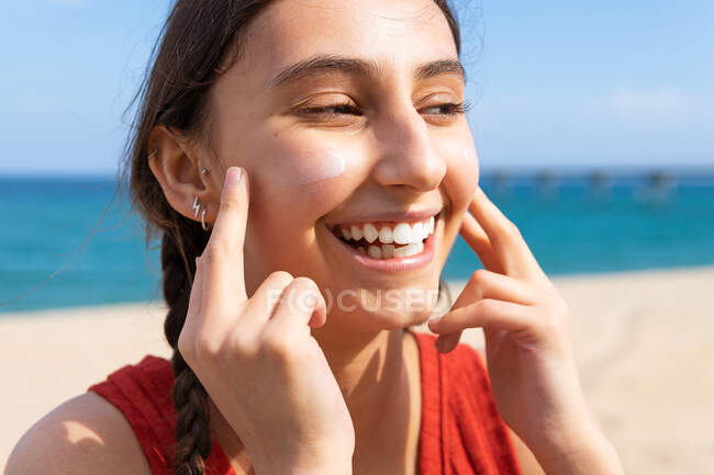 Lächelnde Weibchen cremen sich an sonnigen Sommertagen am Strand mit Sonnencreme ein — Stockfoto