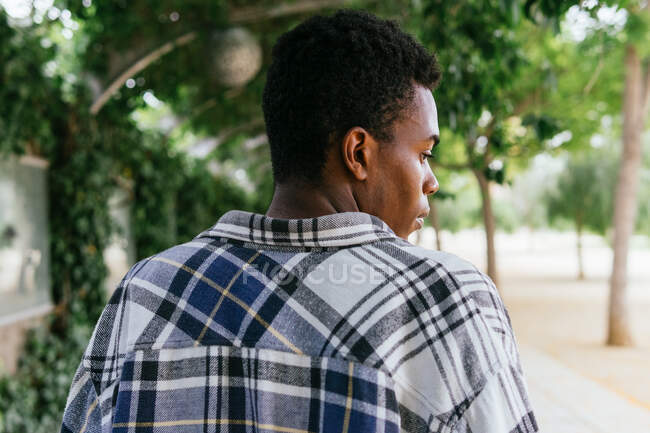 Вид сзади неэмоциональный афроамериканский стильный мужчина, стоящий в городе и смотрящий в сторону — стоковое фото