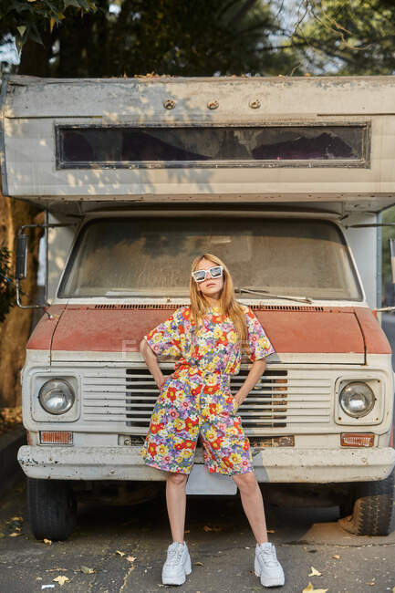 Selbstbewusste Frau im trendigen Sommeranzug steht neben alten verlassenen Wohnwagen und blickt in die Kamera — Stockfoto
