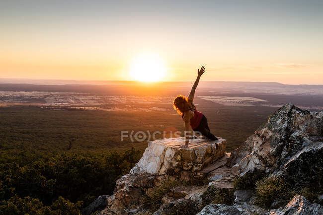 Молода йогиня практикує йогу на скелі в горі зі світлом сходу сонця — стокове фото