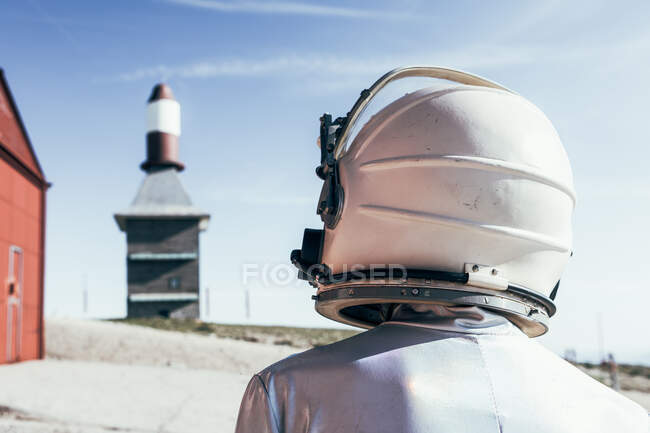 Vista posterior de un traje espacial de pie en suelo rocoso contra las antenas en forma de cohete rayado en el día soleado - foto de stock