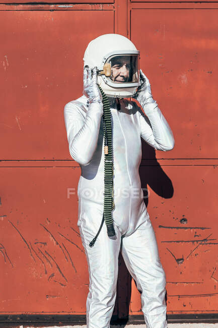 Man in spacesuit standing near red wall of industrial facility on sunny day — Stock Photo