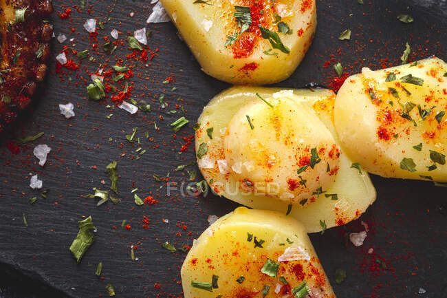Top view of fried octopus tentacle and pieces of potato served with spices on black board on table — Stock Photo