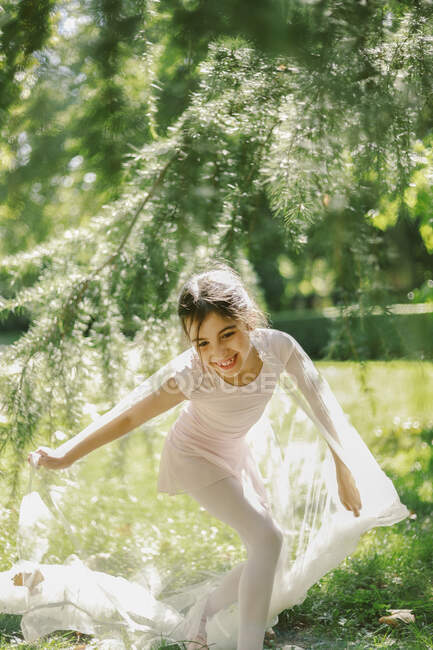 Содержание девушки-подростка в балетном платье и пуантах, играющей с прозрачной тканью на лугу в парке в солнечный день — стоковое фото