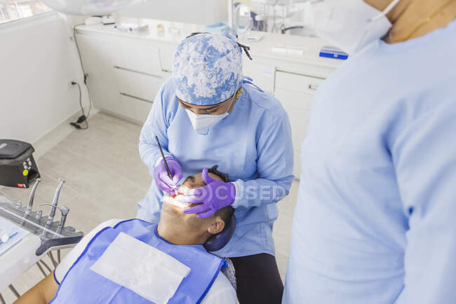 De cima de médico fêmea anônimo em dentes de limpeza uniformes de paciente masculino com retrator dentário no hospital — Fotografia de Stock