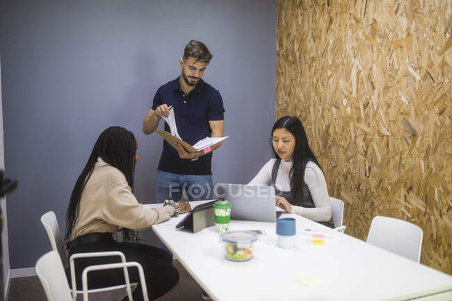 Empresa de colegas multirraciais que se reúnem à mesa e discutem projeto enquanto trabalham juntos no escritório moderno — Fotografia de Stock