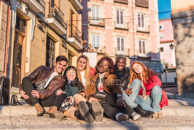 Спільнота багаторасових друзів, які сидять на вулиці і дивляться на камеру в сонячний день — стокове фото