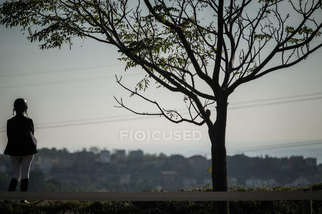 Vista posteriore di equestre anonima che indossa l'uniforme in piedi sul paddock nella zona rurale nella giornata di sole — Foto stock