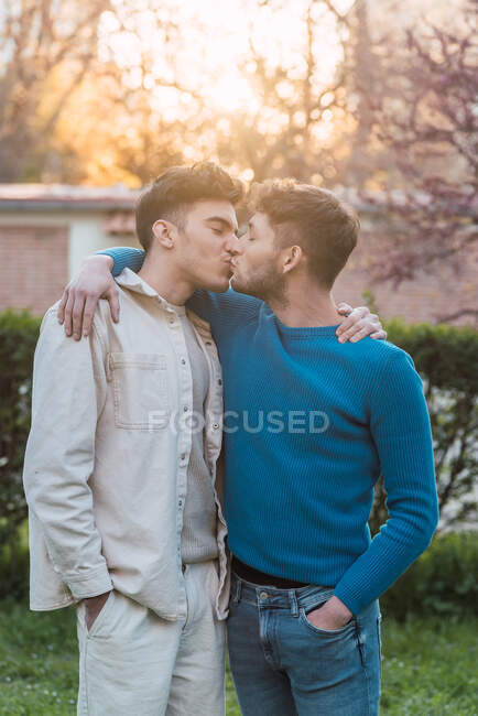 Vista lateral de casal homossexual encantado de homens beijando e olhando um para o outro no parque — Fotografia de Stock