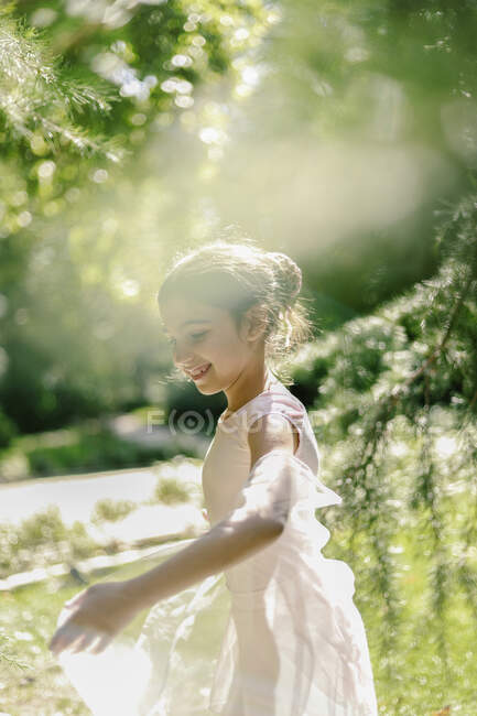 Zufriedene Teenagerin im Ballettkleid spielt an sonnigem Tag mit transparentem Tuch auf Wiese im Park — Stockfoto