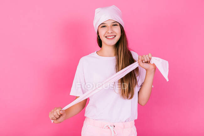 Adolescente feminina despreocupada em vestuário casual com cabelo castanho e lenço de cabeça representando consciência conceito olhando para a câmera em pé sobre fundo rosa — Fotografia de Stock