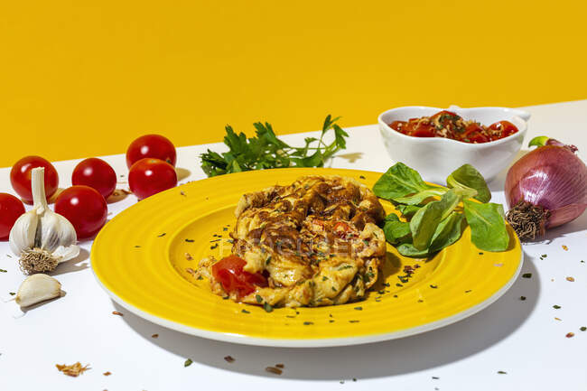 Köstliche Omelette mit gehackter Petersilie auf Teller gegen sonnengetrocknete Tomaten und rohe rote Zwiebel auf weißem Hintergrund — Stockfoto