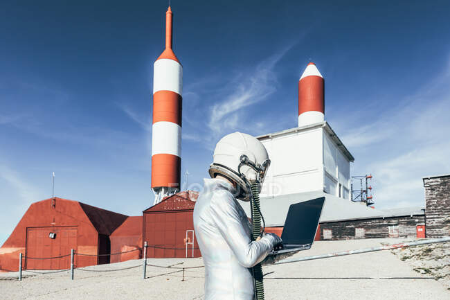 Vista lateral astronauta masculino no traje espacial que navega dados no netbook enquanto está fora da estação com antenas em forma de foguete — Fotografia de Stock
