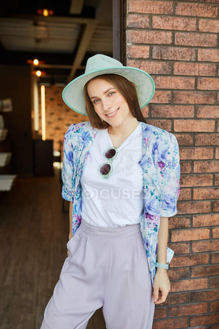 Cheerful young female in trendy wear looking at camera against rough wall in town — Stock Photo