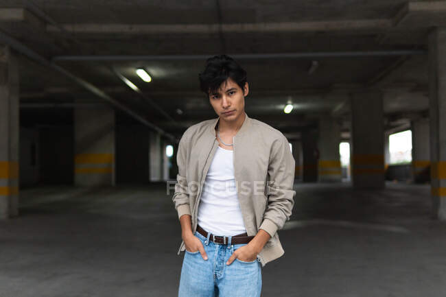 Портрет молодого латинця в повсякденному одязі впевнено дивиться на камеру з руками на кишенях, стоячи на парковці — стокове фото