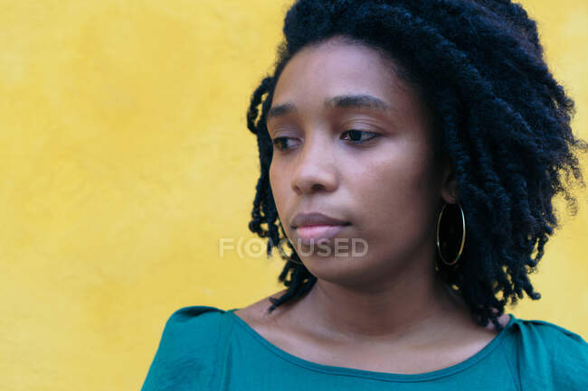 Retrato de una joven afro-mujer pensativa frente a una pared amarilla - foto de stock