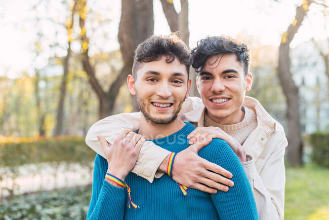 Cheerful LBGT couple of men embracing while standing in park and looking at camera — Stock Photo