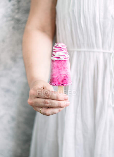 Femme sans visage en robe de lin offrant yaourt à la mûre maison popsicle avec garniture blanche — Photo de stock